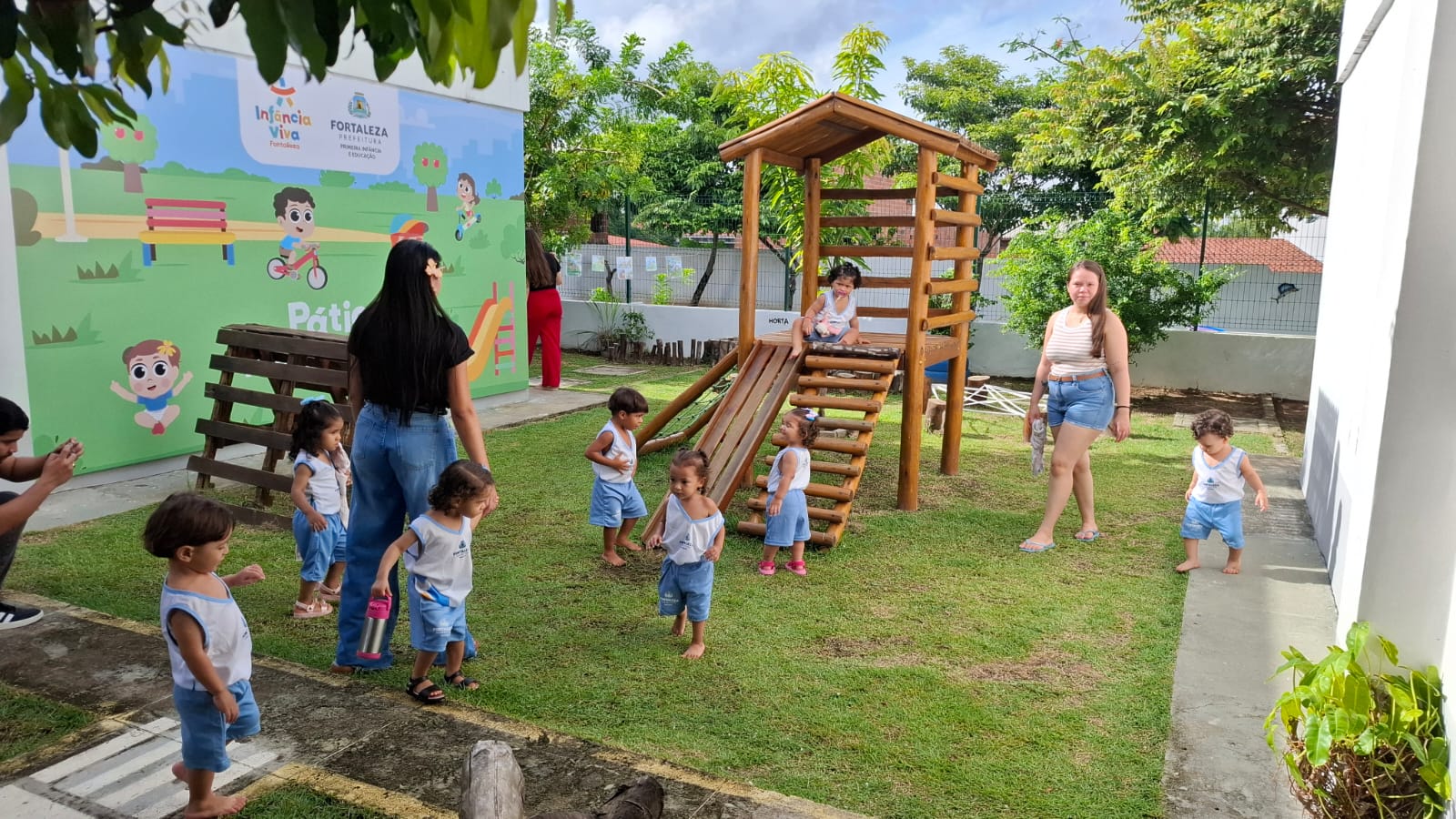 crianças brincando num espaço gramado com brinquedos de madeira num centro de educação infantil